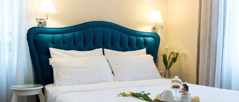 Un lit bien fait, avec une tête de lit de couleur turquoise, une literie blanche et une table de chevet surmontée d’une lampe.