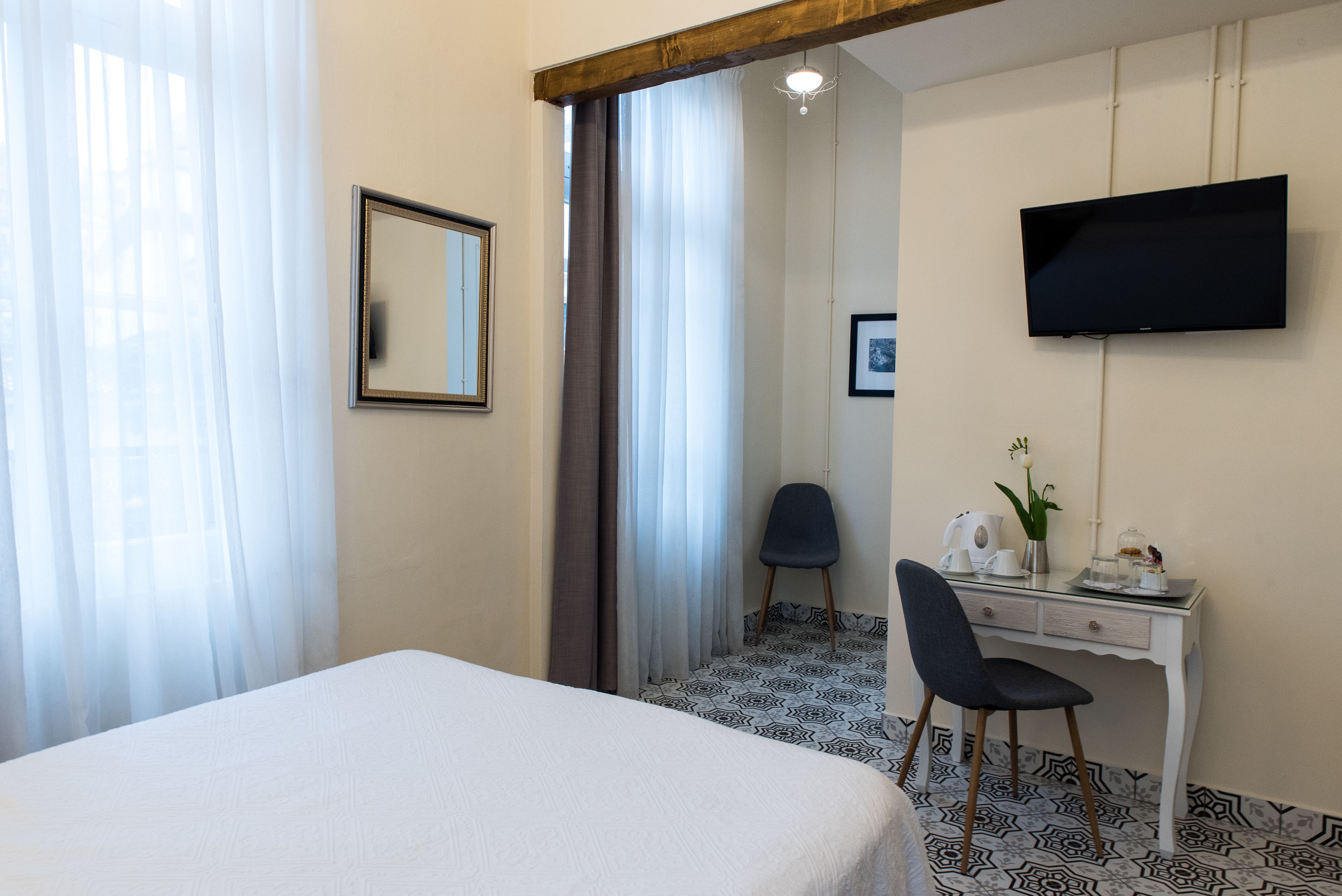 A hotel room with a bed, a desk with a chair, a television, and a window with curtains.