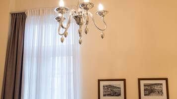 Un candelabro, una ventana con cortinas de gasa y dos cuadros en la pared.