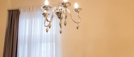 Un candelabro, una ventana con cortinas de gasa y dos cuadros en la pared.
