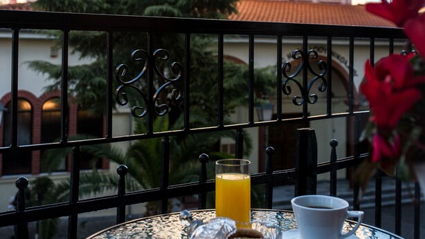 A table with a glass of orange juice and a cup of coffee, a decorative glass, and a flower.