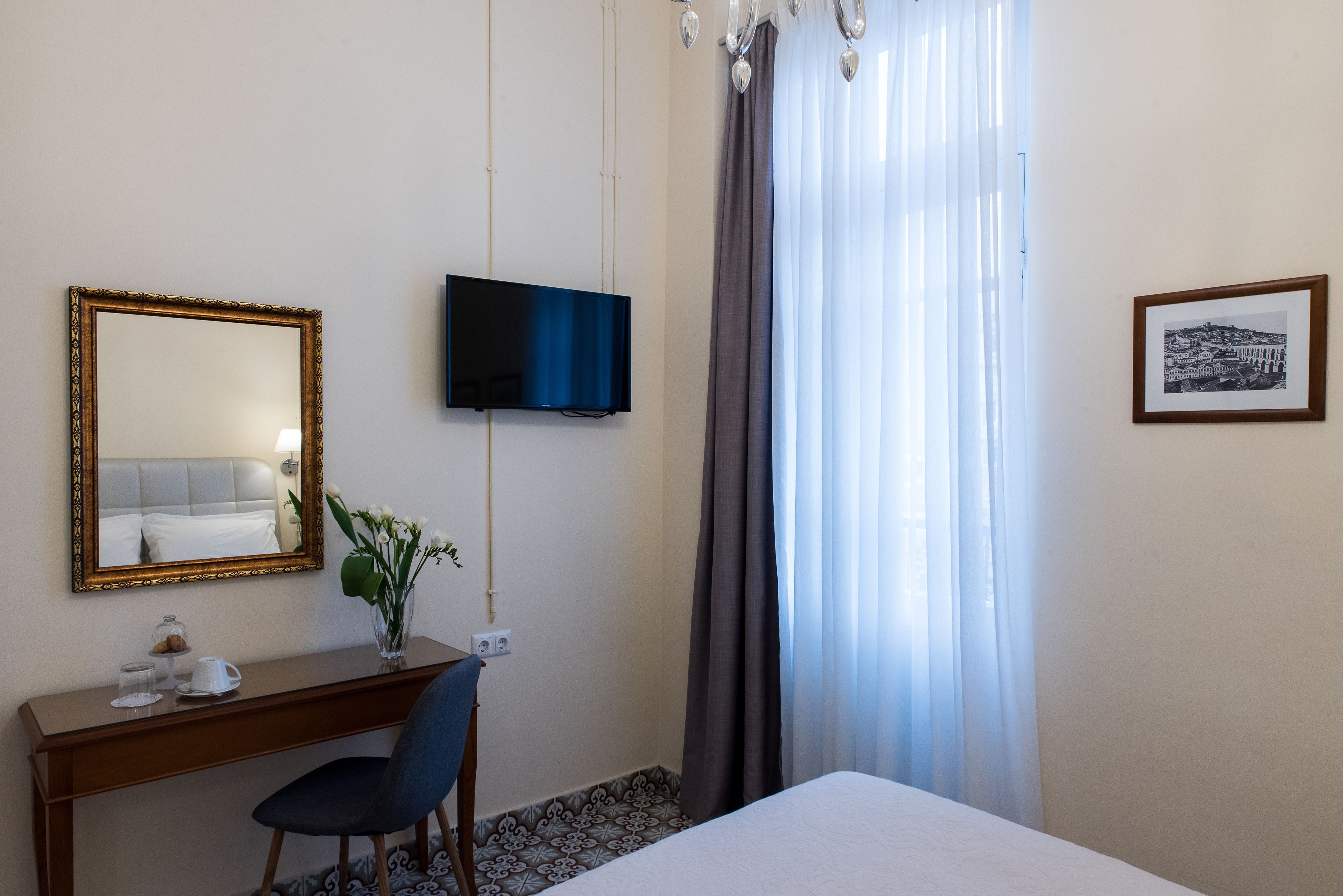 Una camera d'albergo con un letto, una scrivania con una sedia, una televisione, uno specchio e un quadro appeso al muro.