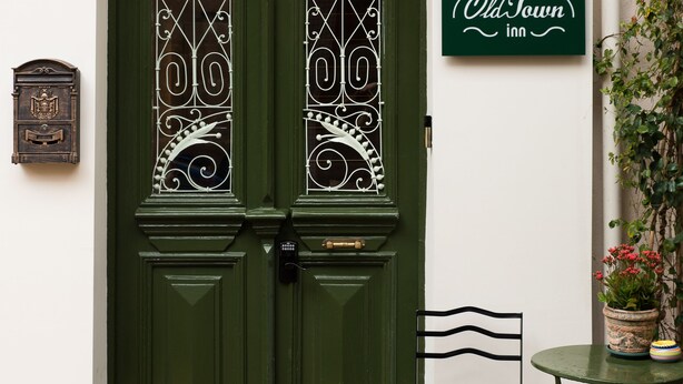 A green double door with intricate metalwork, a small table with a potted plant, and a sign for 'OldTown Inn' on the wall.