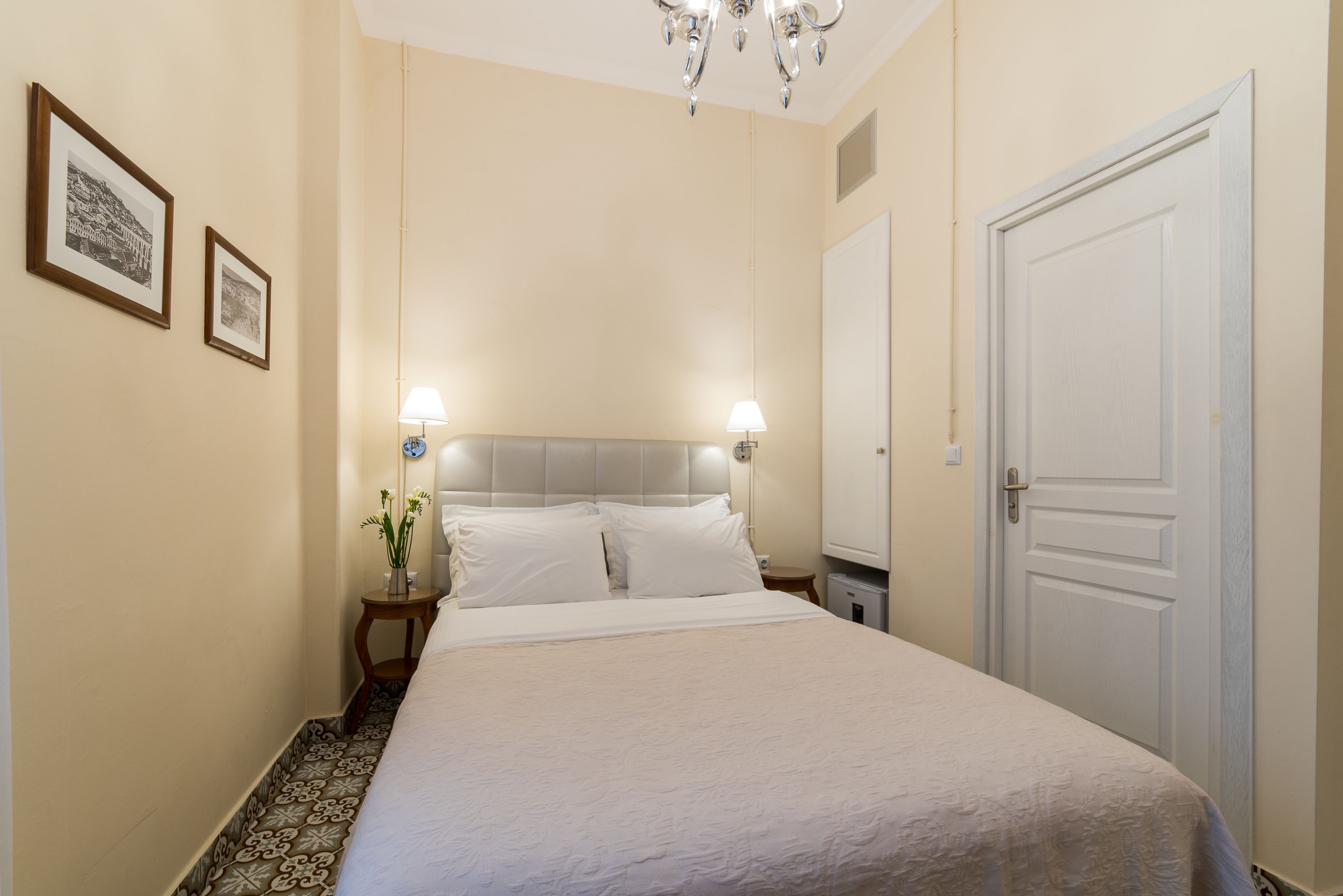 Une chambre à coucher bien rangée, avec un lit, deux tables de chevet, une commode, une lampe et une porte.