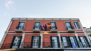 A red building with multiple balconies, flags, and a year plaque.