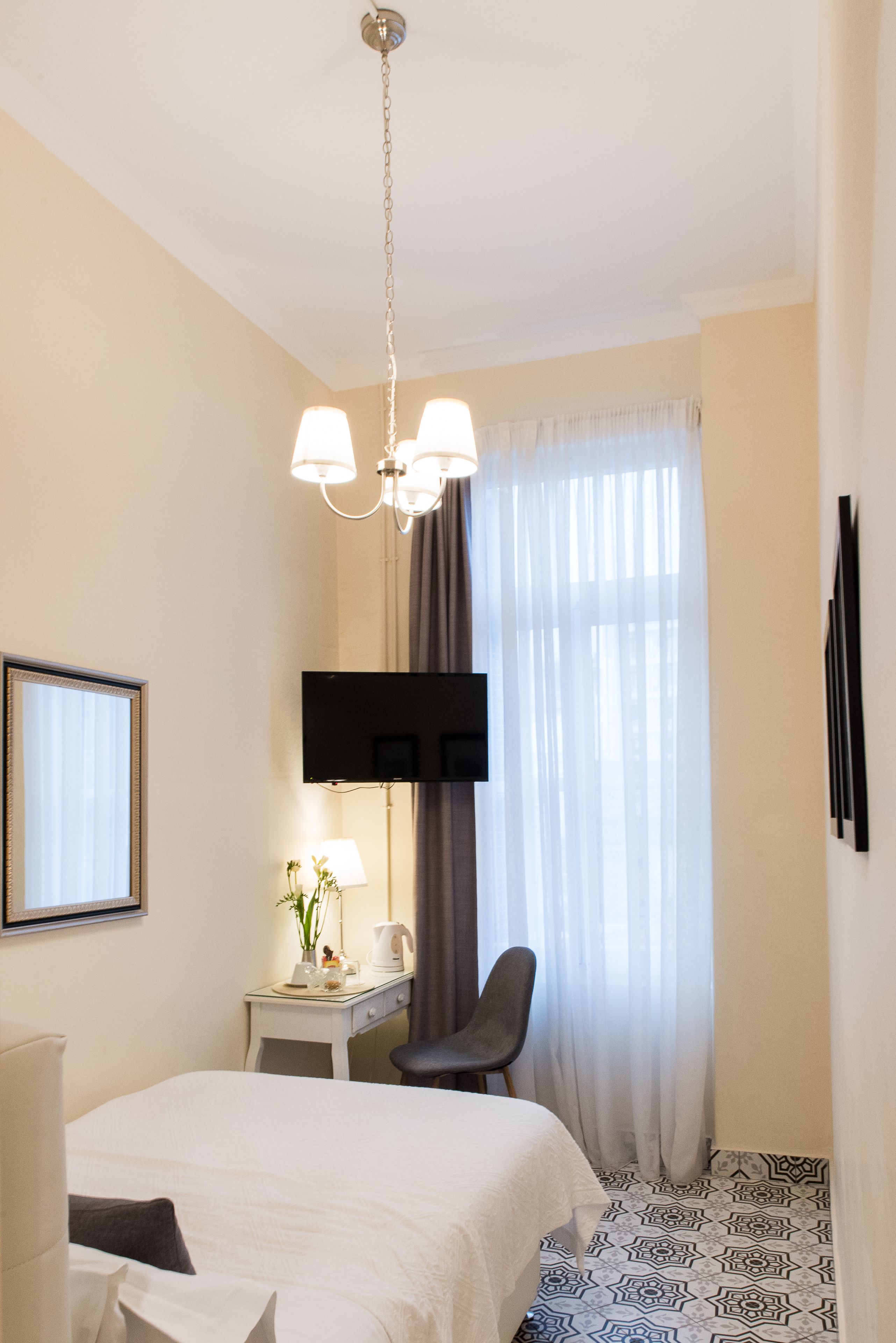 Habitación de hotel con cama, escritorio con silla, televisor montado en la pared y ventana con cortinas.