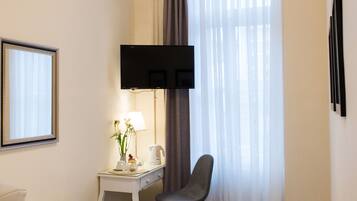 Habitación de hotel con cama, escritorio con silla, televisor montado en la pared y ventana con cortinas.