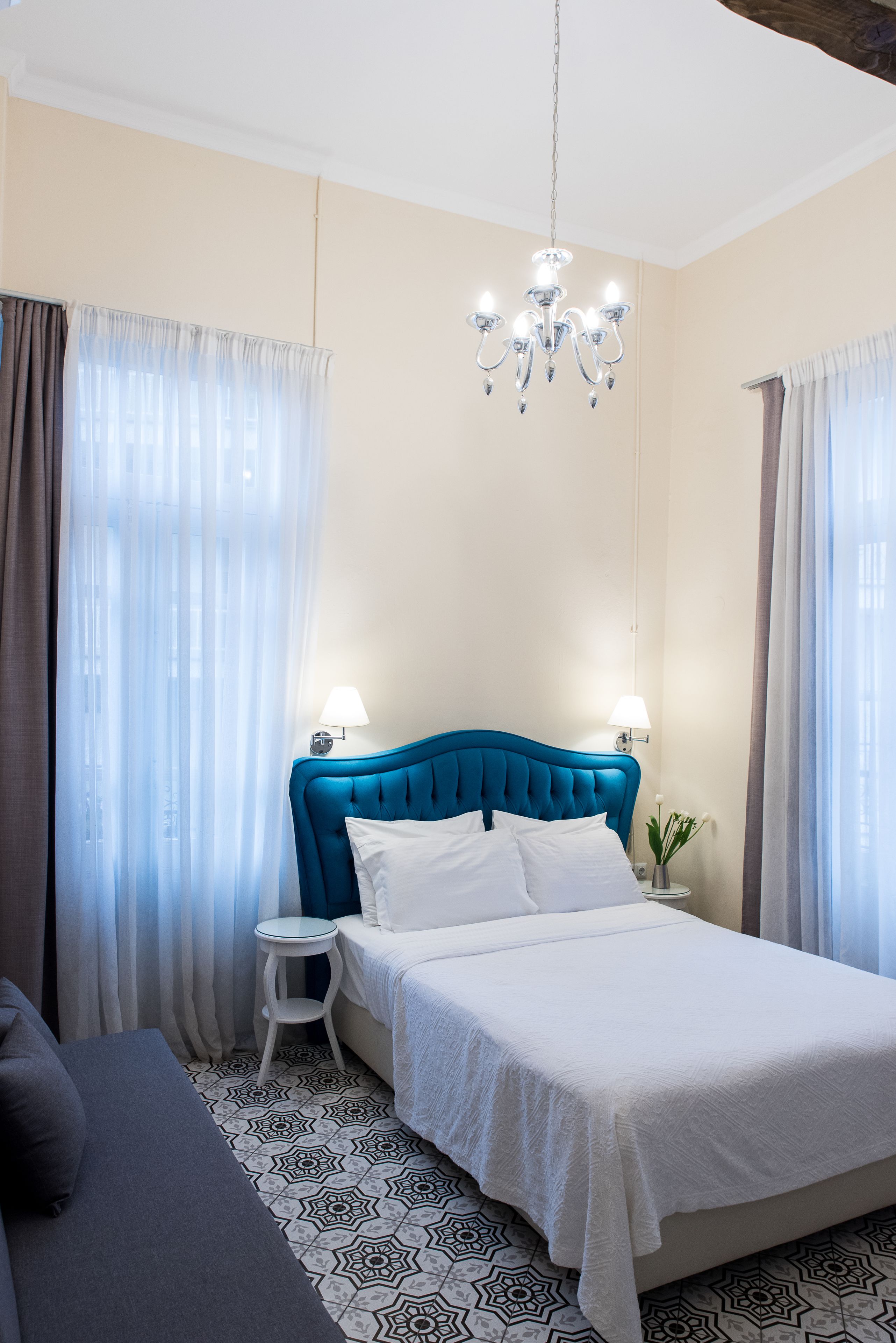 Une chambre à coucher avec une tête de lit bleue, un couvre-lit blanc, une table de chevet avec une lampe et un petit tabouret blanc.