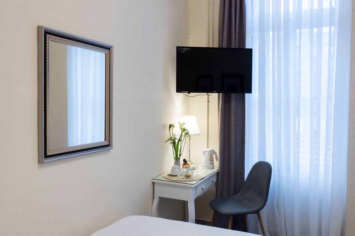 Habitación de hotel con cama, escritorio con lámpara, silla, televisión de pantalla plana y un espejo grande.
