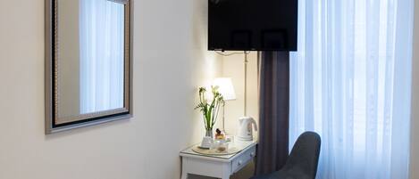 Habitación de hotel con cama, escritorio con lámpara, silla, televisión de pantalla plana y un espejo grande.