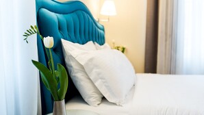 A neatly made bed with white bedding, a teal headboard, and a small table with a vase of flowers.
