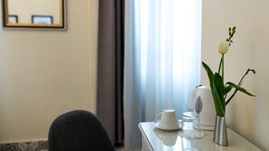 A hotel room with a table set for tea, a white flower vase, and a kettle.