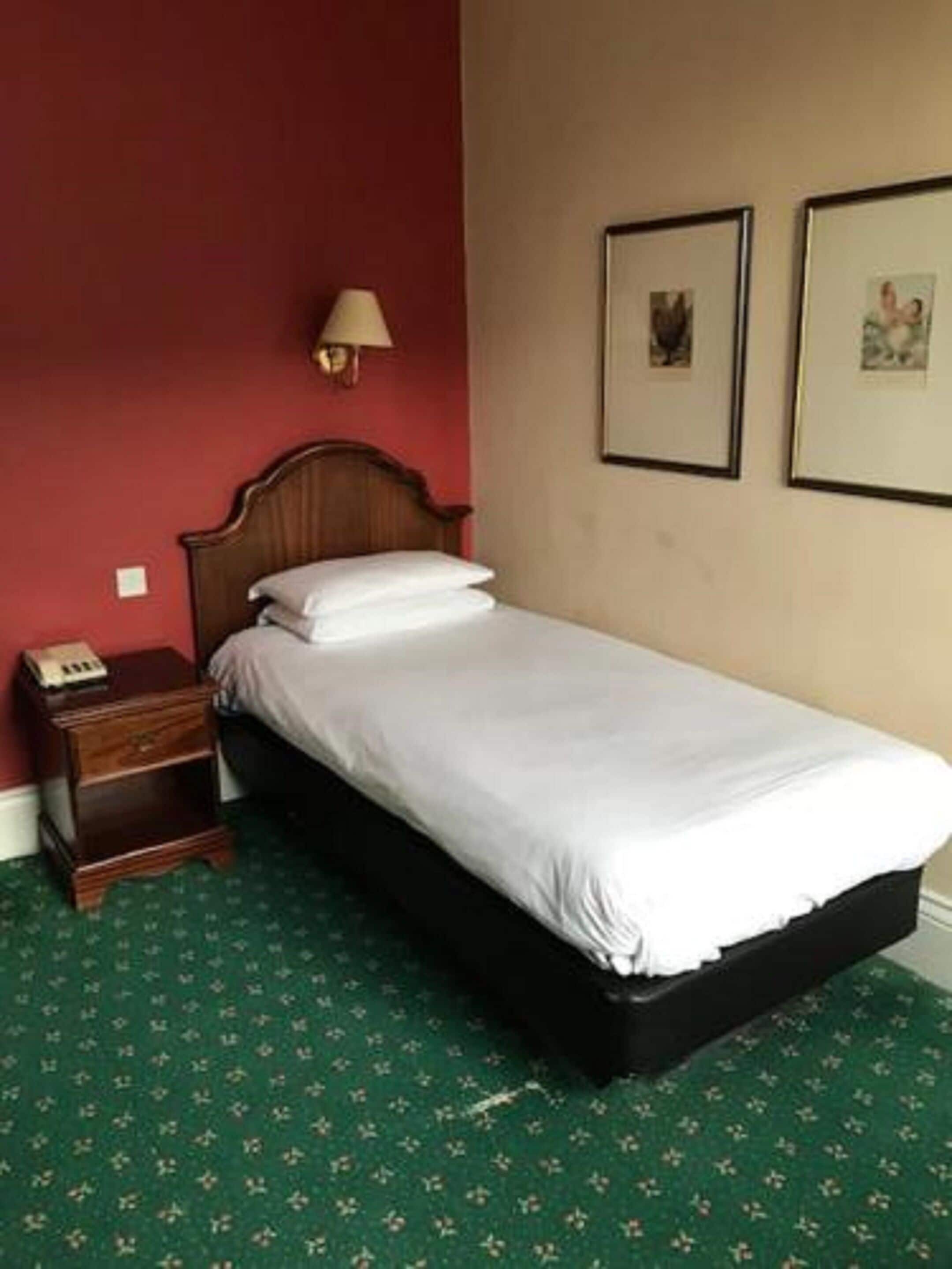 Un letto rifatto con lenzuola bianche in una stanza con parete rossa e tappeto verde.