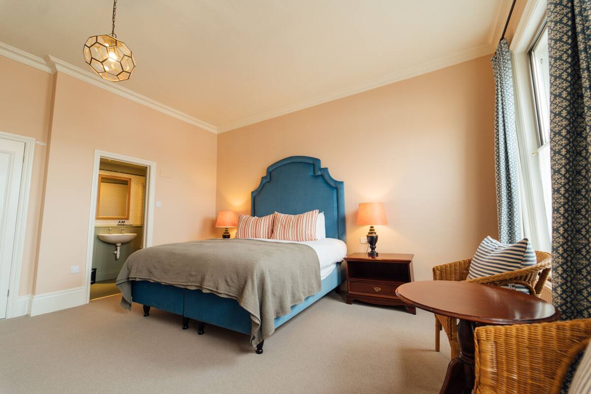 Un dormitorio con cama, mesitas de noche, una silla, una lámpara y un candelabro.