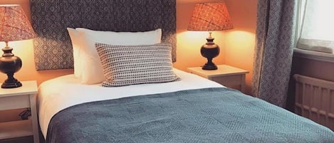 A neatly made bed with a patterned headboard, two bedside lamps, and a window with curtains.