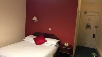 Habitación de hotel con cama, mesita de noche con teléfono, lámpara de pared y puerta con cerradura.