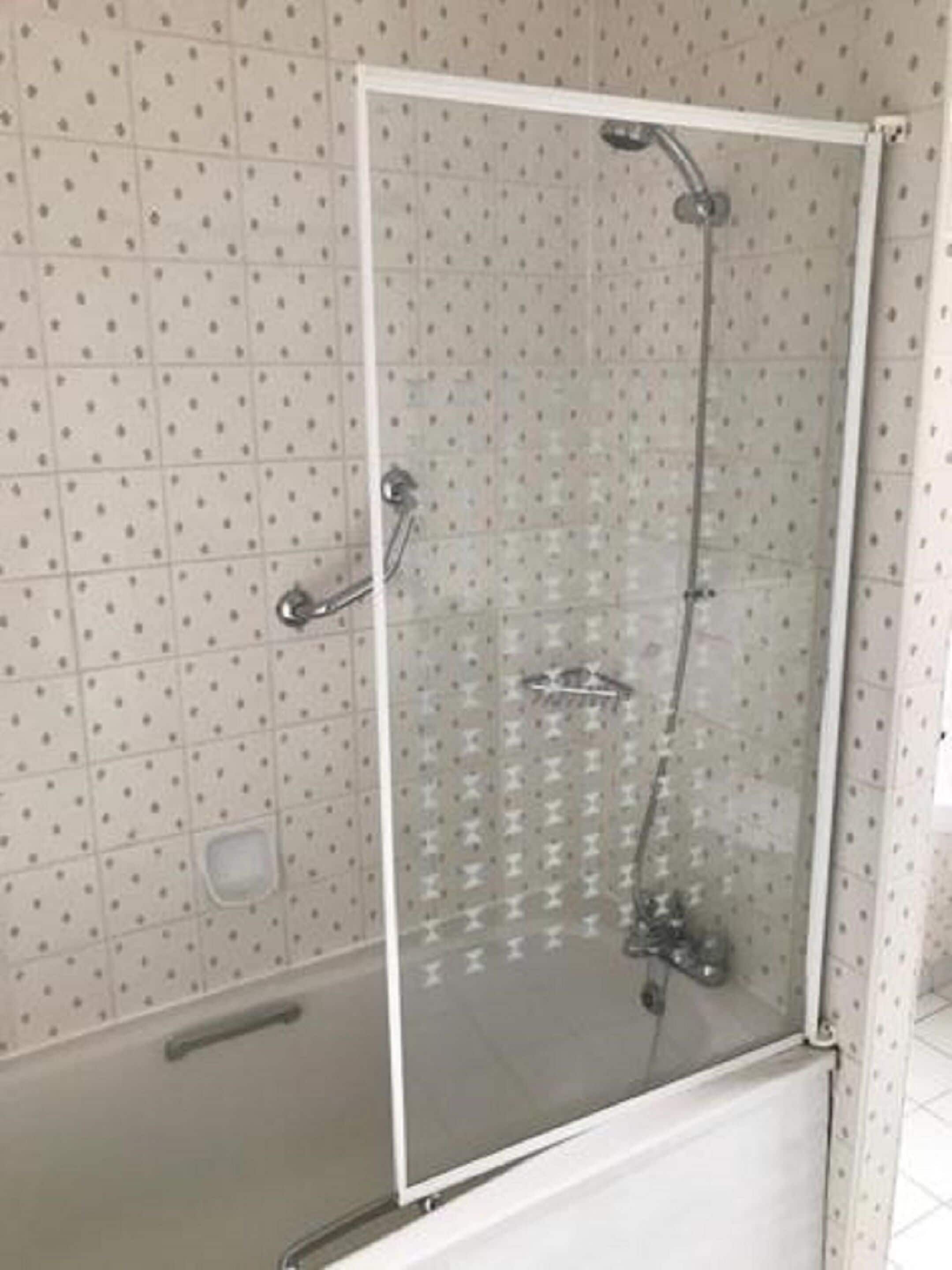 A glass-enclosed shower with a handheld showerhead and a fixed overhead showerhead.