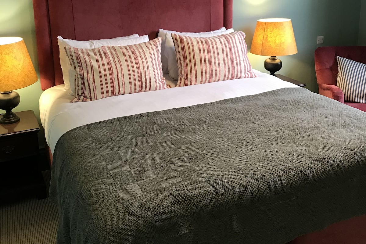 Una cama con cabecera roja, ropa de cama blanca y almohadas a rayas. Hay dos lámparas de noche y una silla con una almohada a rayas.