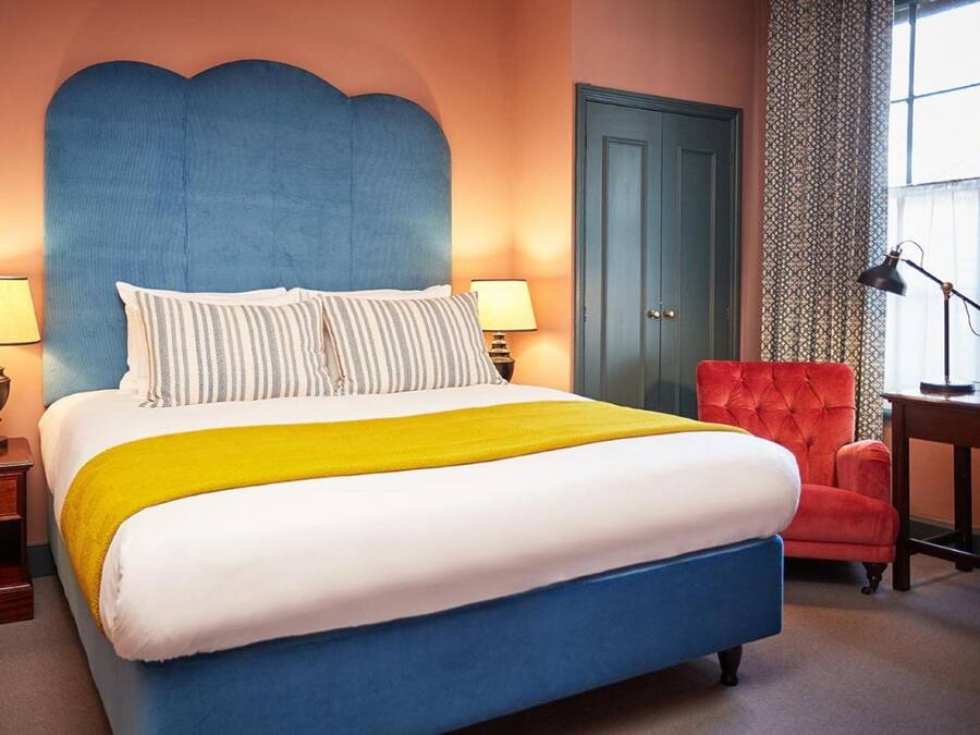 Un dormitorio con una cama grande, dos lámparas de noche, un sillón rojo y un escritorio con lámpara.