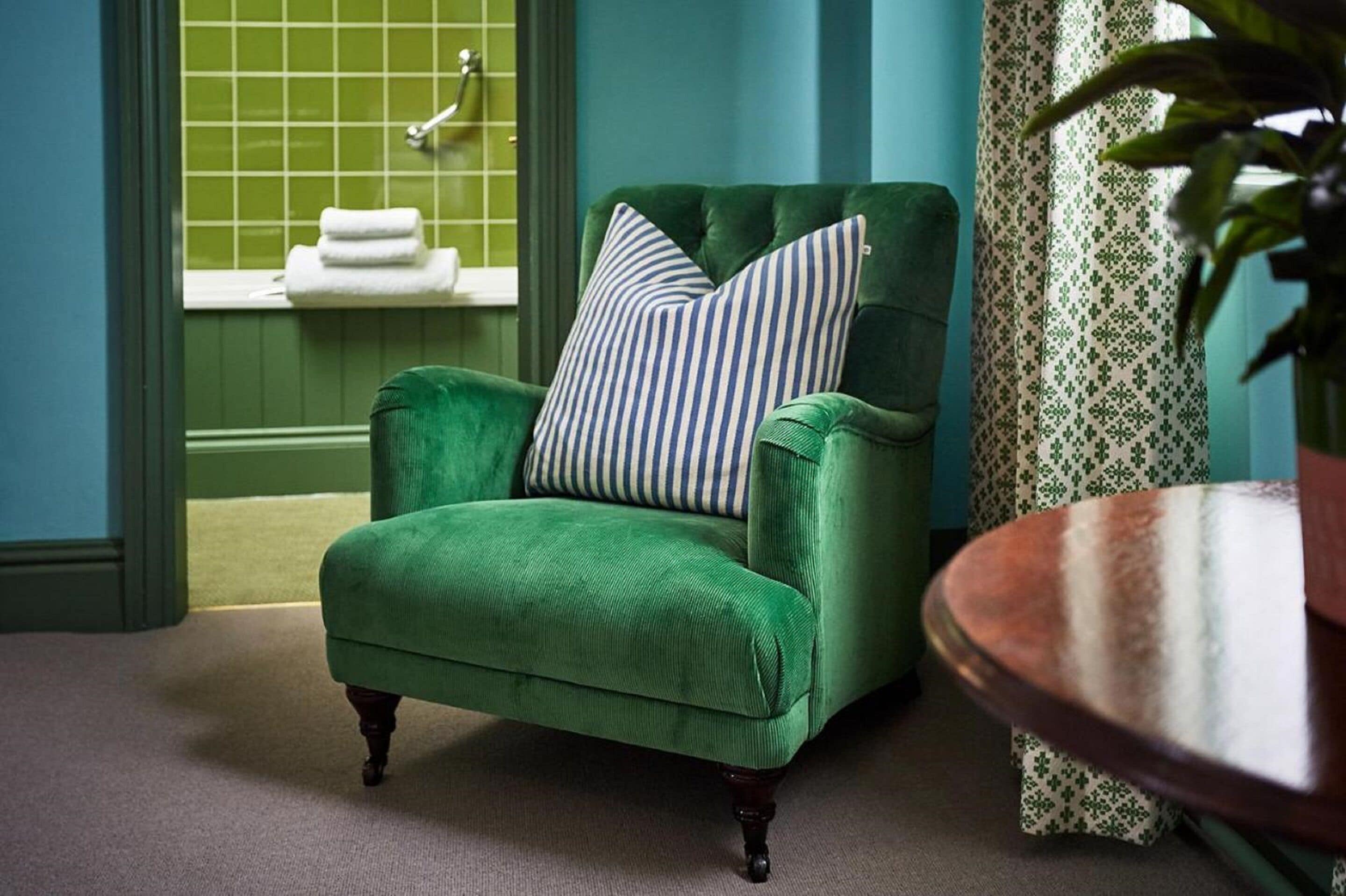 A green armchair with striped pillows in a room with teal walls and a green tiled shower area.