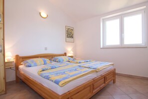 Een tweepersoonsbed met houten frame, twee nachtkastjes met lampen, een raam met zonwering, en een wandlamp.