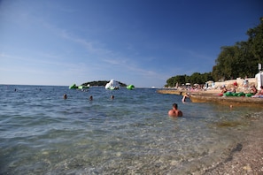 A beach scene with clear water, people swimming, and green inflatable boats. - Sea view, 300m to the beach, 3 bedrooms, 2 bathrooms, washing machine / dishwasher (Porec)