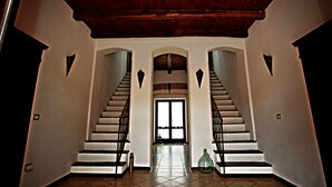 A grand staircase with a wooden ceiling and white walls, leading to a door with a view outside. - Is Scabas (Solarussa)