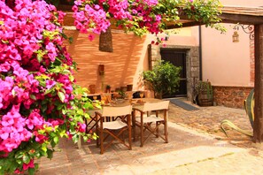 An outdoor patio with a table and chairs, surrounded by vibrant pink flowers and potted plants. - Is Scabas (Solarussa)