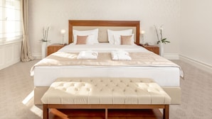 Een keurig opgemaakt slaapkamer met een groot bed, nachtkastjes, een bankje en twee planten in potten.