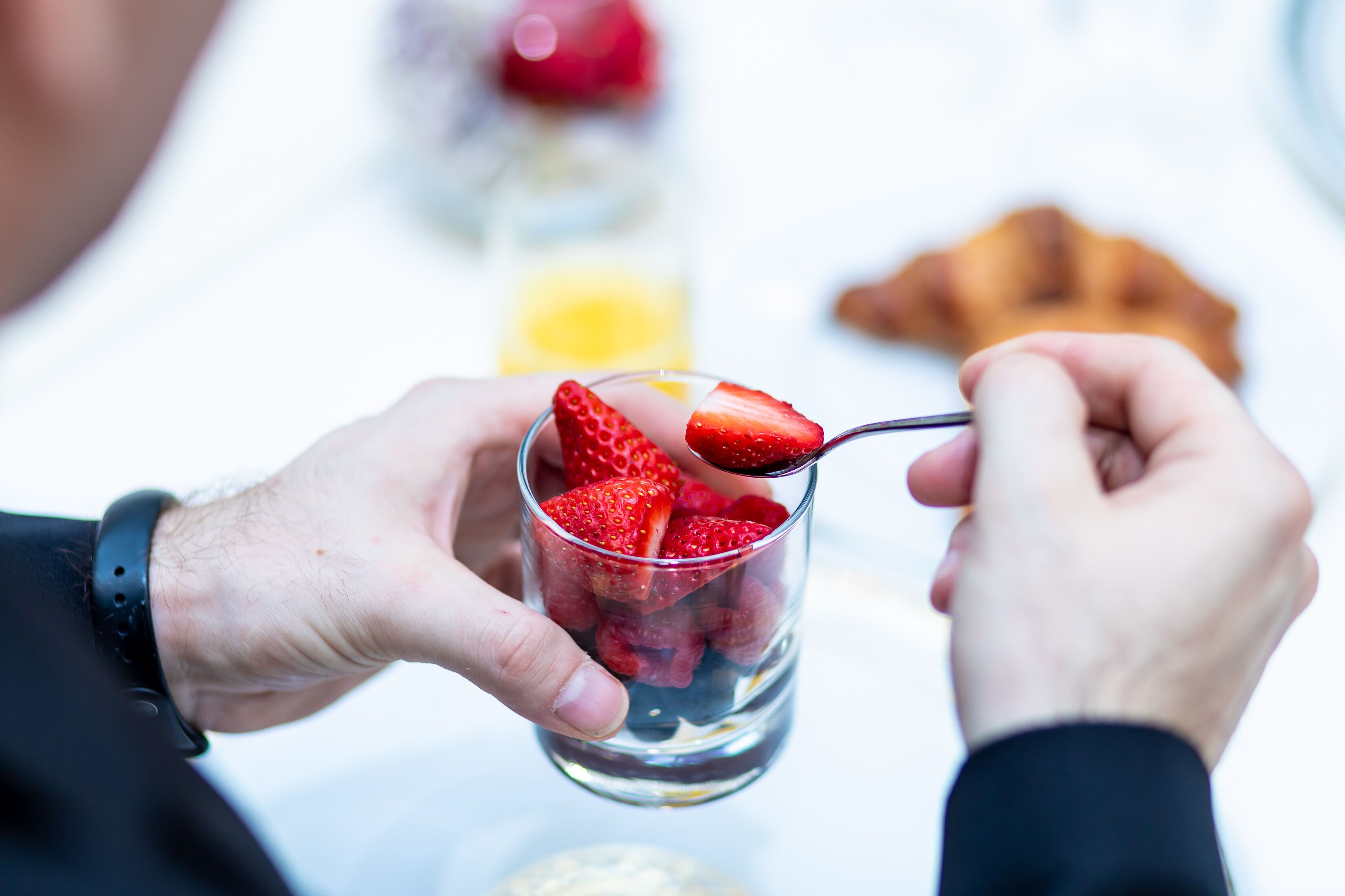 Une personne tenant un verre contenant des fraises et une cuillère.