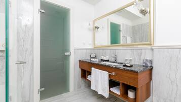 A bathroom with a glass shower door, a wooden vanity with a marble countertop, a large mirror, and a towel rack.
