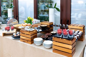 A buffet setup with various food items and beverages, wooden serving stations, and potted plants. - Le Premier Boutique Hotel (Zagreb)