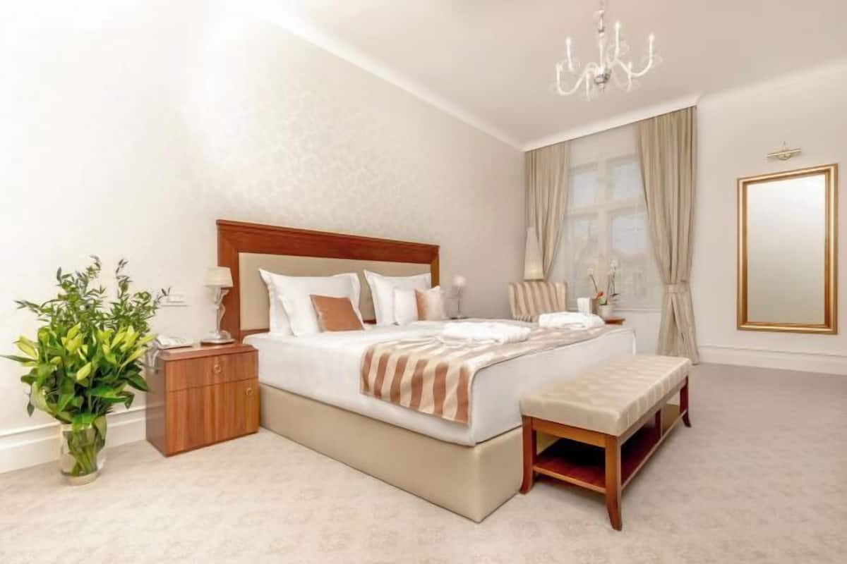 Een slaapkamer met een bed, nachtkastje, bankje en een plant.