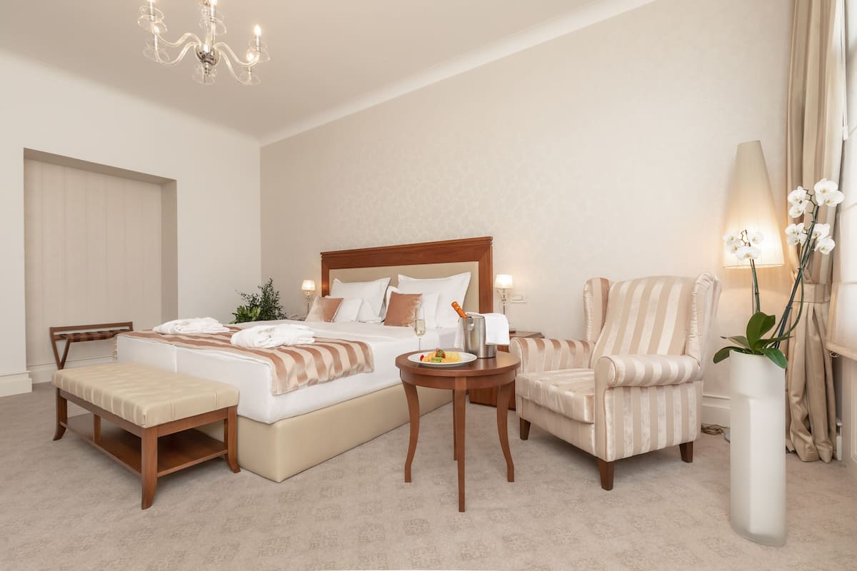 Een hotelkamer met een groot bed, een nachtkastje, een stoel, een bankje, een lamp en een potplant.