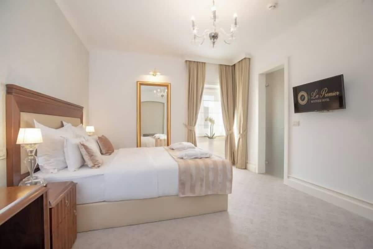 Een slaapkamer met een bed, nachtkastje, spiegel, kroonluchter en een bord aan de muur.