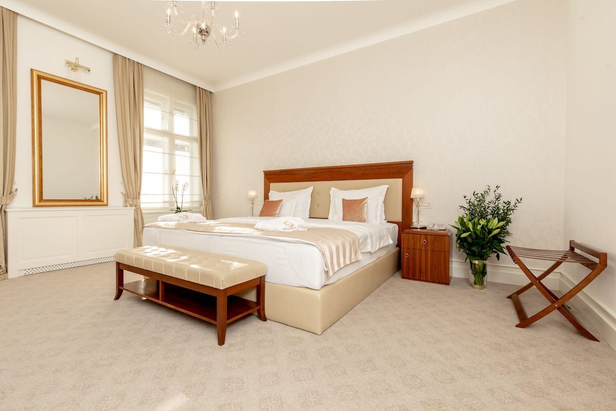 Een slaapkamer met een groot bed, nachtkastjes, een bankje, een spiegel en een plant.