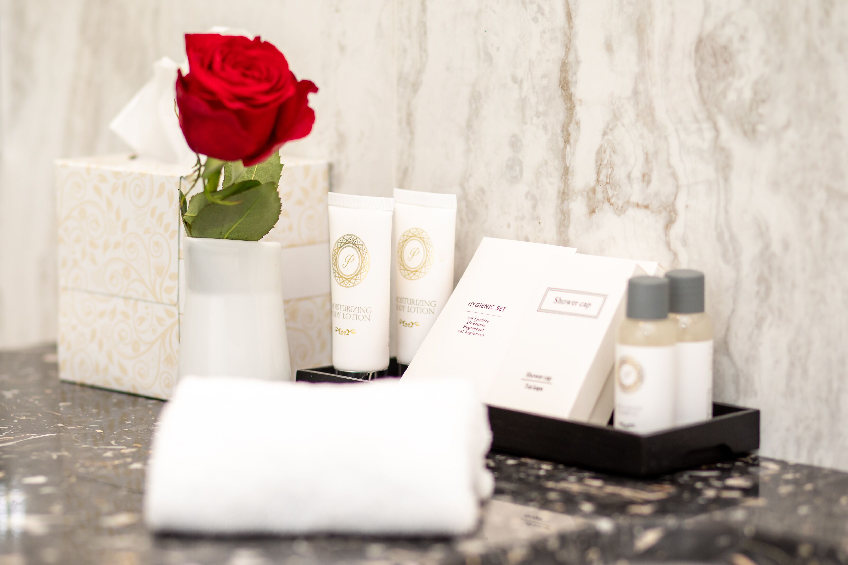 A bathroom vanity with toiletries, a tissue box, and a red rose.