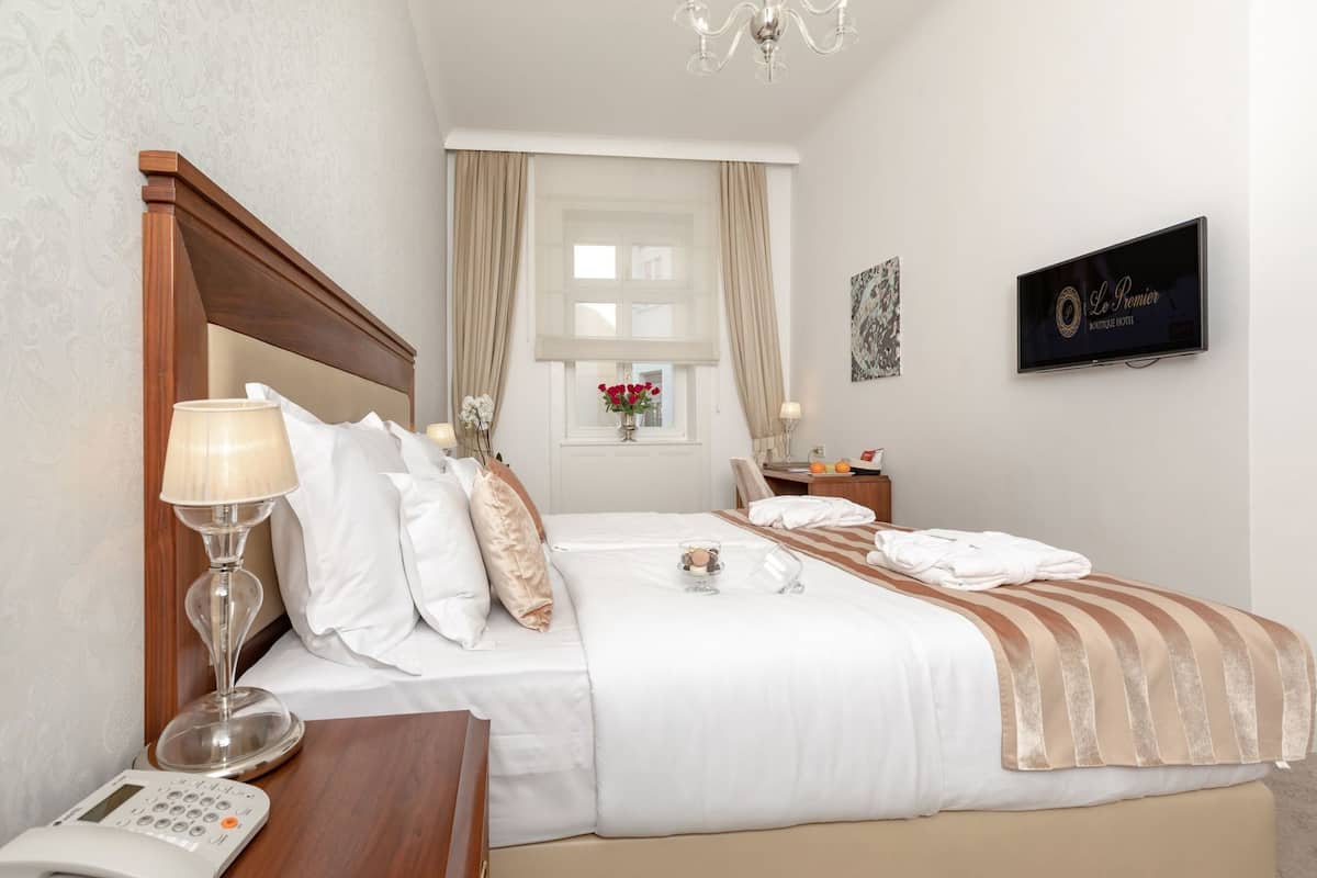 Een hotelkamer met een bed, nachtkastje, lamp en een televisie aan de muur.