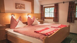 A neatly made bed with checkered bedding, a wooden headboard, and a window with plaid curtains. - Ferienwohnung Hochkalter, 1-2 Erwachsene + 1 Kind, 40 qm, Dusche/WC, TV, W-LAN, Ostbalkon, 1 Schlafzimmer, Nichtraucher (Ramsau bei Berchtesgaden)