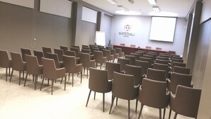 Un salón de conferencias con filas de sillas, un atril y una pantalla de presentación.