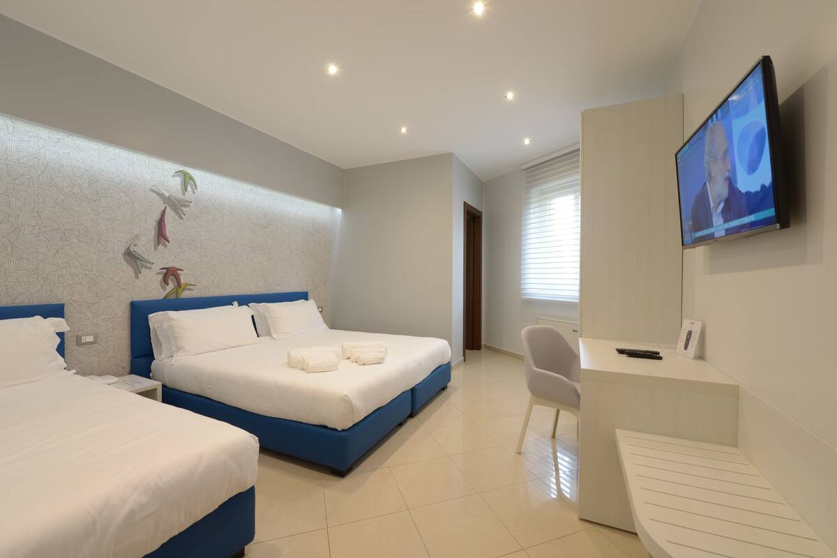 Ein Hotelzimmer mit zwei Betten, einem Schreibtisch, einem Stuhl, einem Fernseher und einer Wand mit Muster.