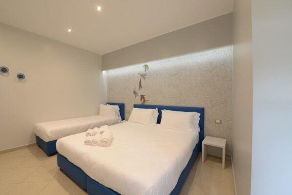 A hotel room with two beds, a small bedside table, and a wall-mounted light fixture. - Imperiali Hotel (Francavilla Fontana)