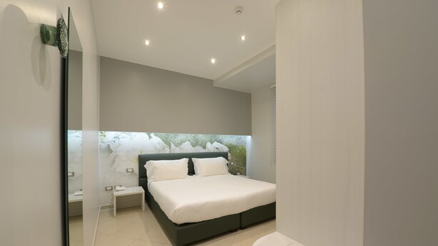 Un dormitorio moderno con cama, mesitas de noche y vistas a la vegetación a través de una ventana.