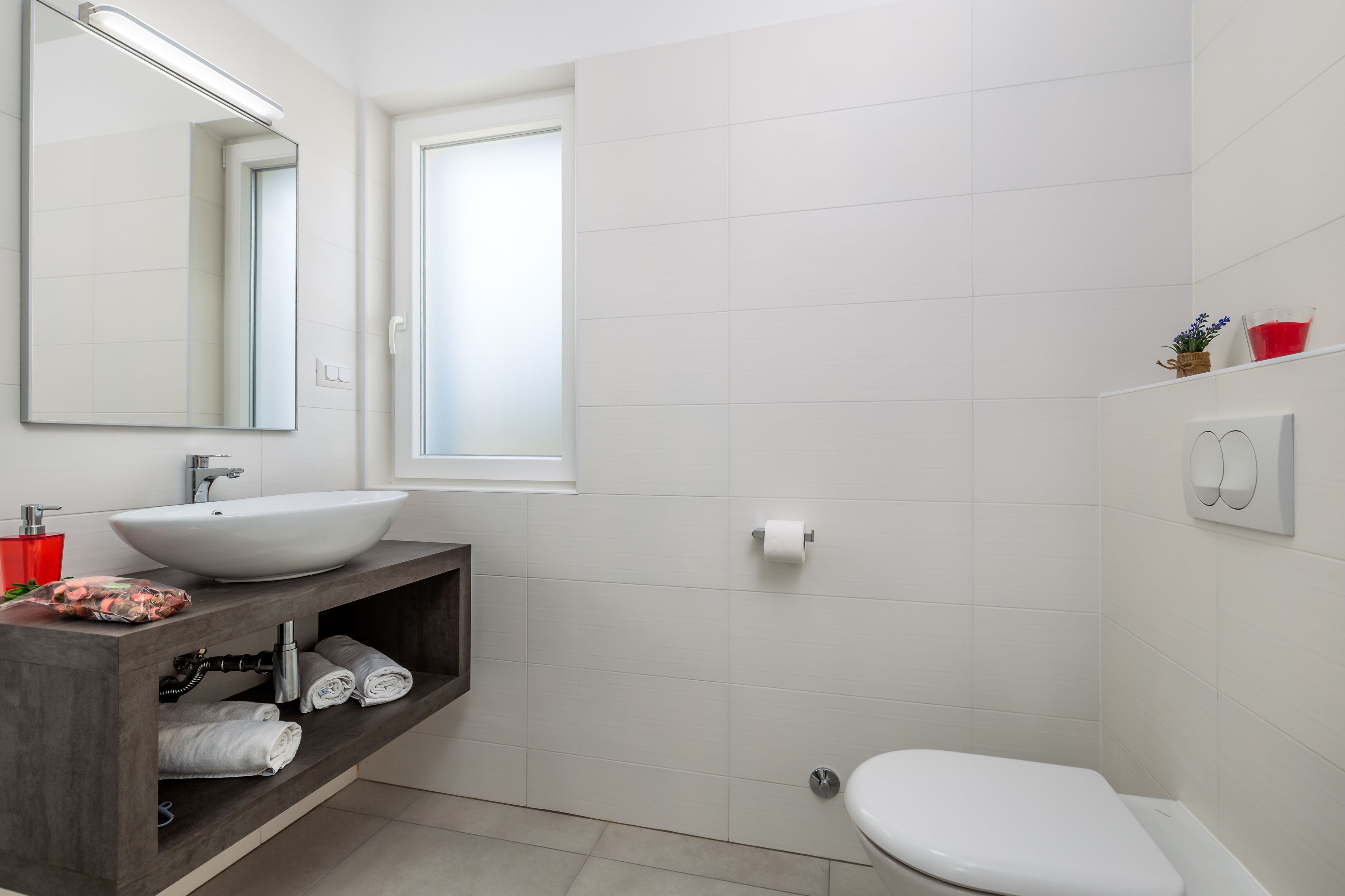 A modern bathroom with a large mirror, white sink, and a toilet.
