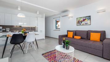 Ein modernes Wohnzimmer mit einem grauen Sofa, orangefarbenen Kissen, einem weißen Couchtisch mit Pflanze und einem farbenfrohen Teppich.