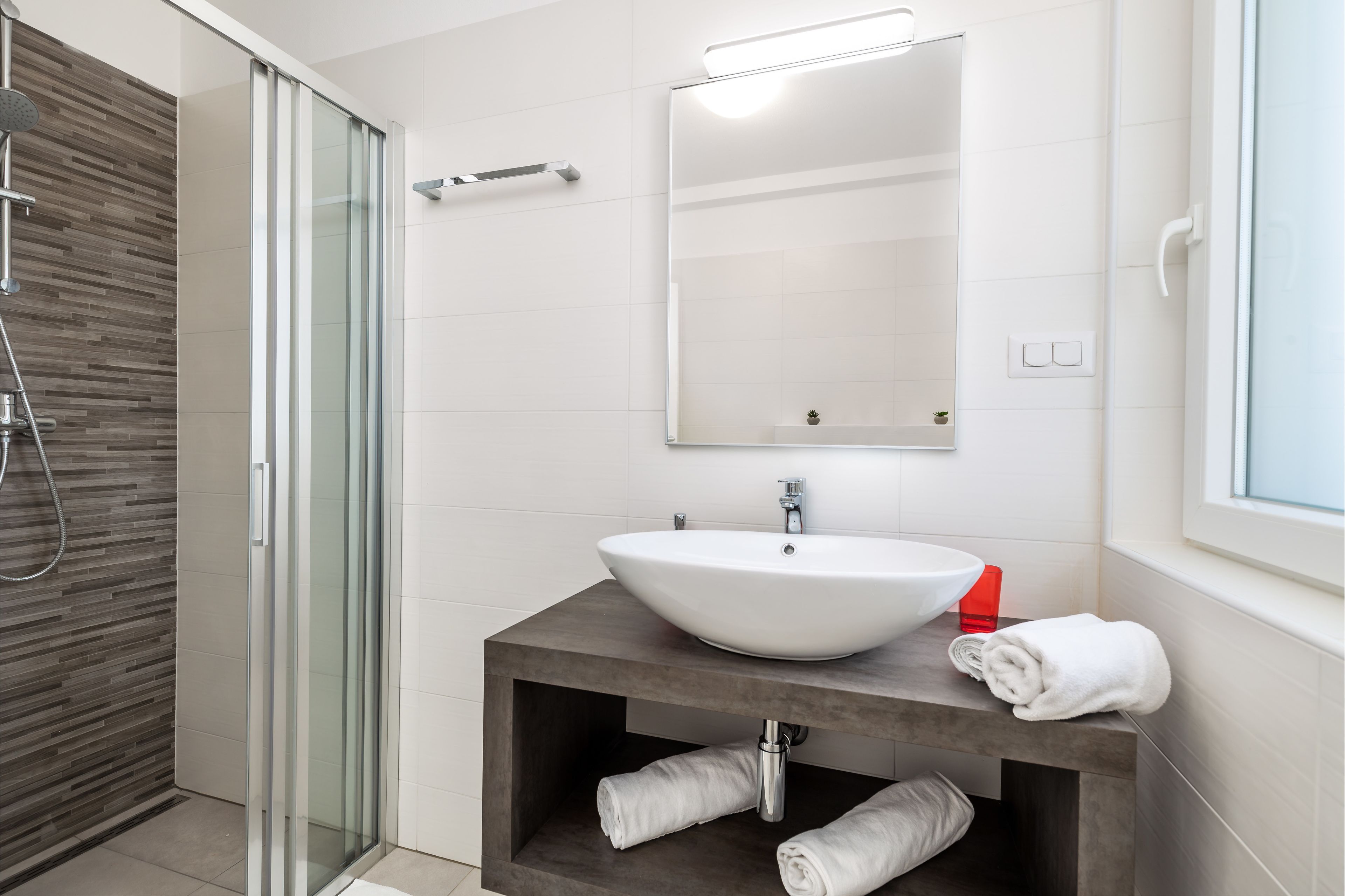 A modern bathroom with a glass shower enclosure, a white sink with a wooden vanity, and a large mirror above the sink.