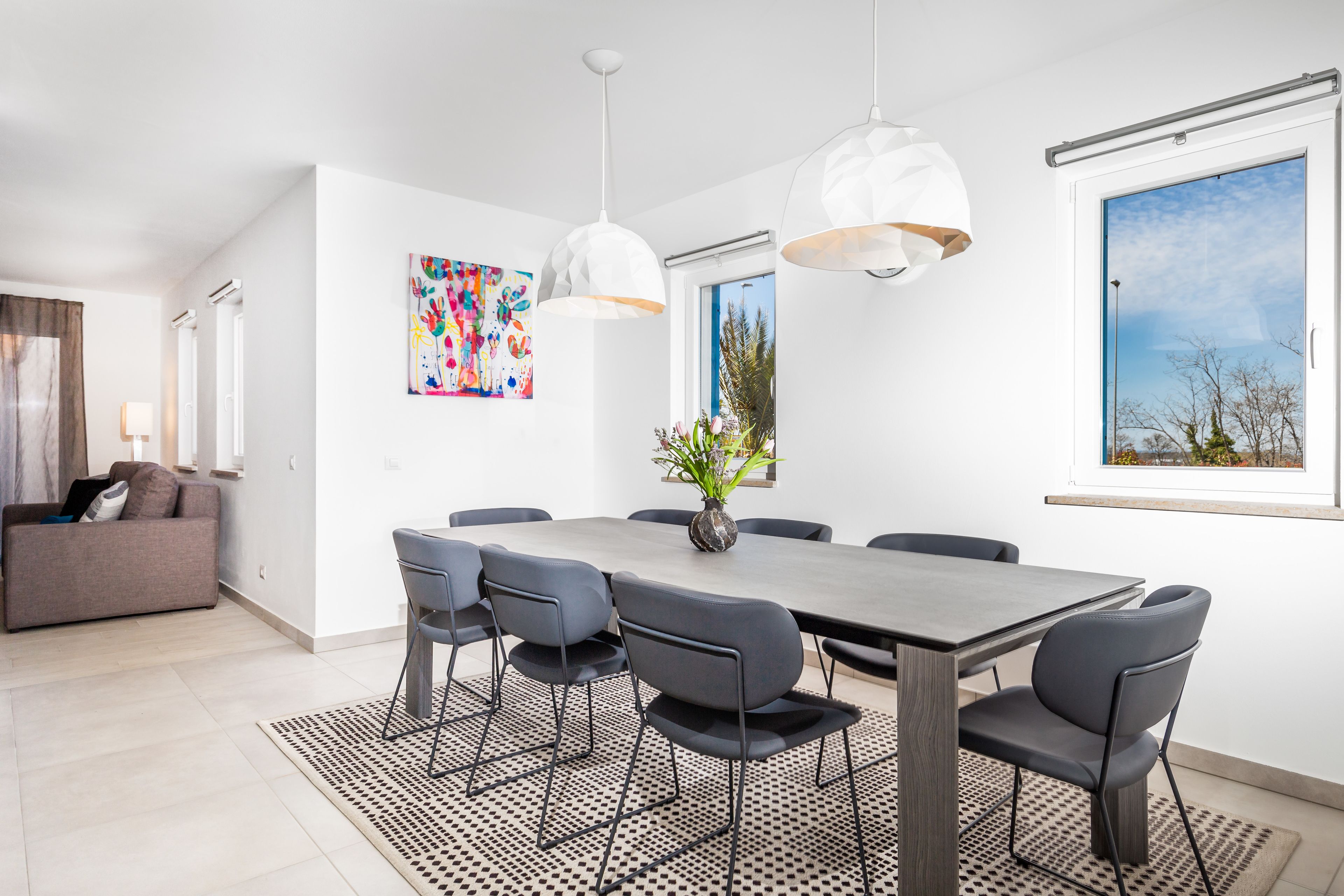 A modern dining area with a large table, six chairs, and pendant lighting.