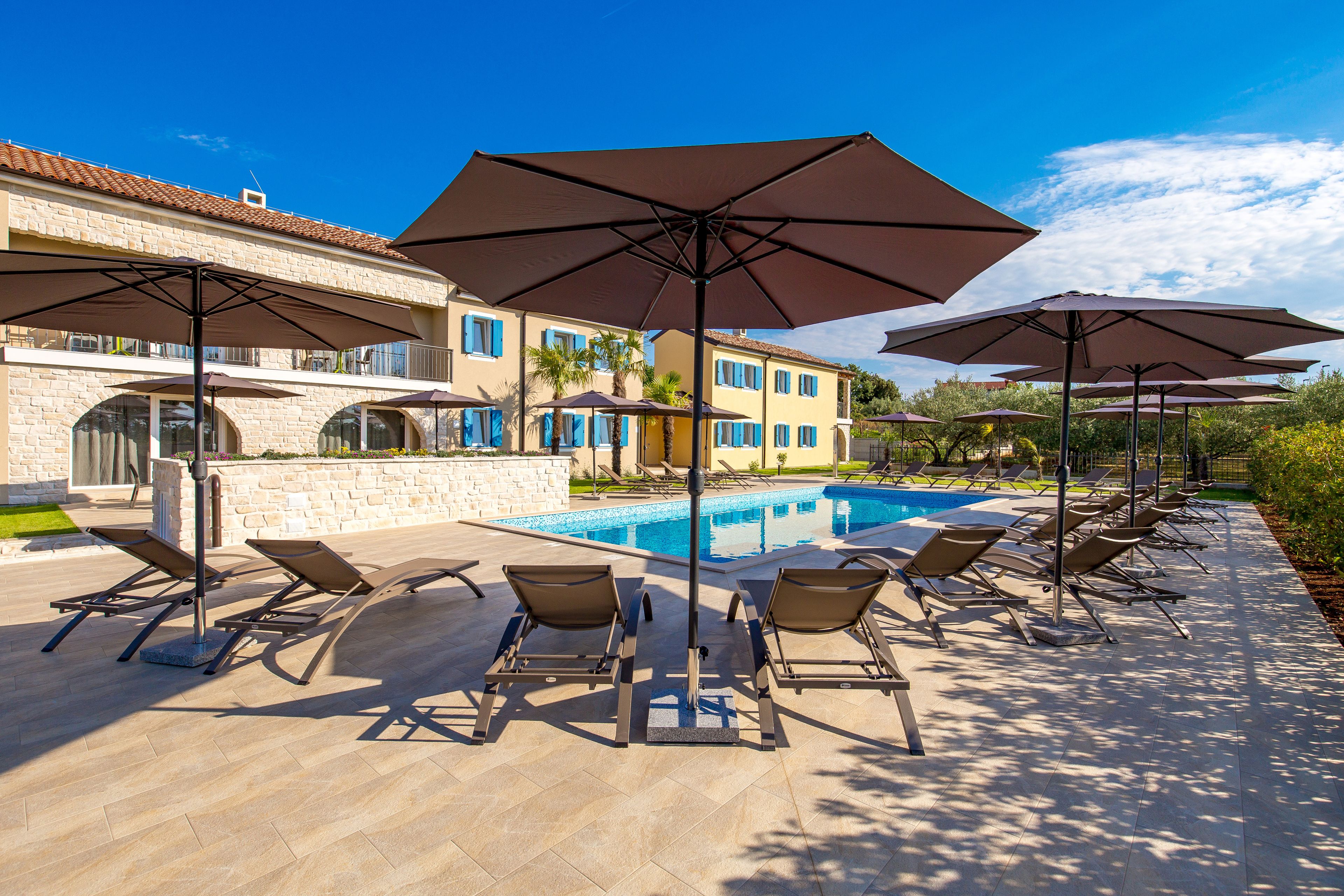 A poolside area with lounge chairs and umbrellas, a swimming pool, and a building with a tiled roof.