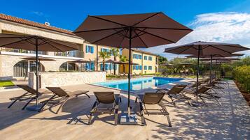 A poolside area with lounge chairs and umbrellas, a swimming pool, and a building with a tiled roof.