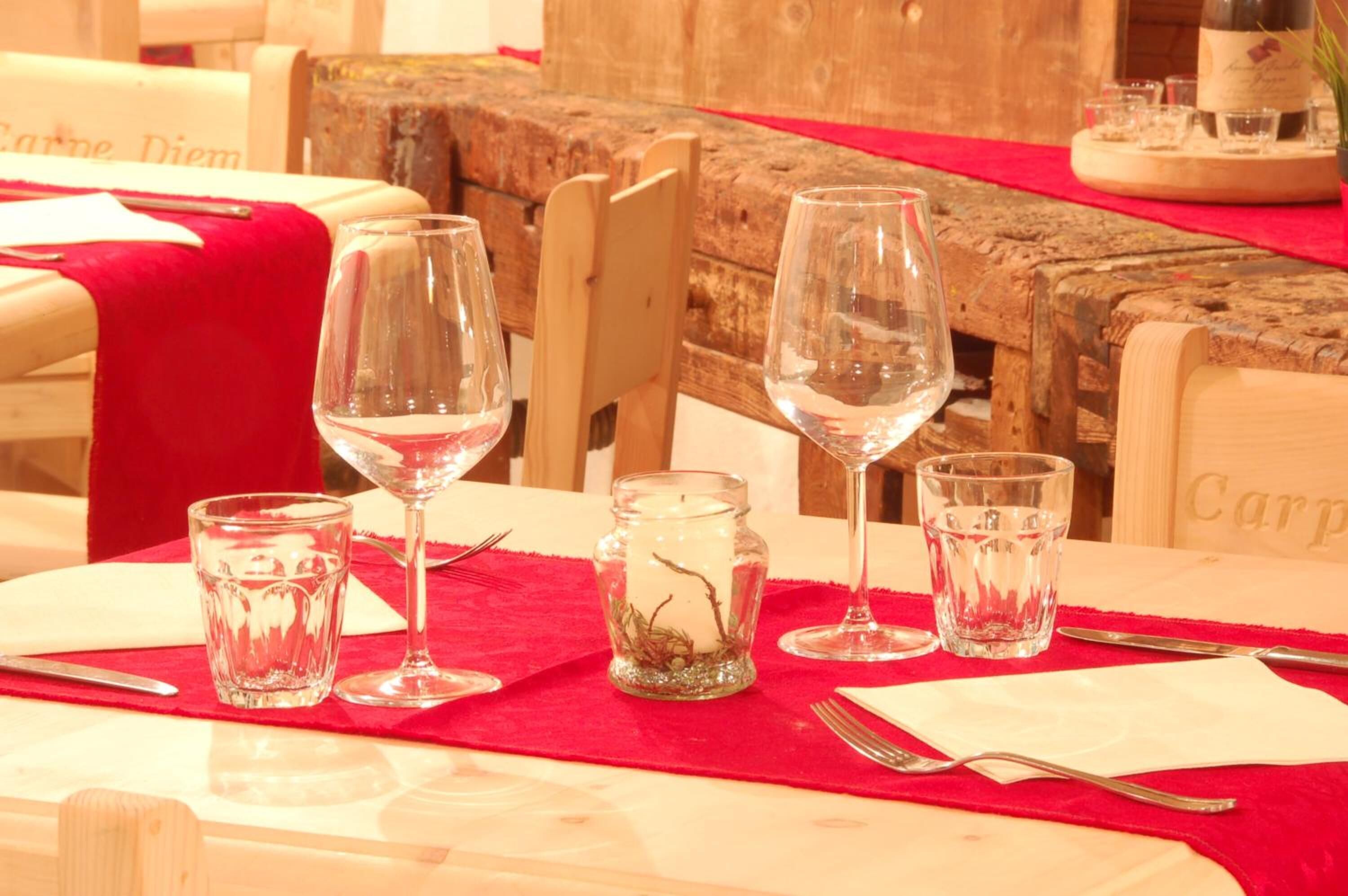 Una mesa de comedor dispuesta con copas de vino, vasos de agua y una vela en un tarro de cristal.